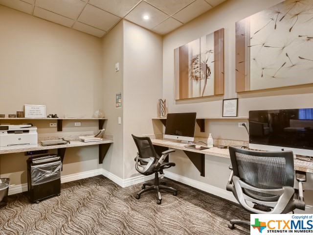 carpeted office with a paneled ceiling and built in desk