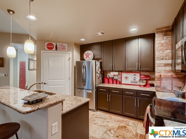 kitchen featuring stainless steel appliances, light stone countertops, a kitchen bar, hanging light fixtures, and dark brown cabinets