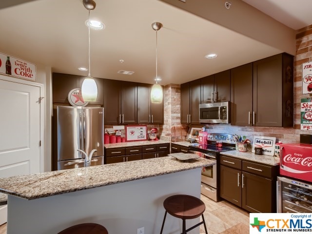 kitchen with light stone counters, stainless steel appliances, decorative light fixtures, beverage cooler, and a center island