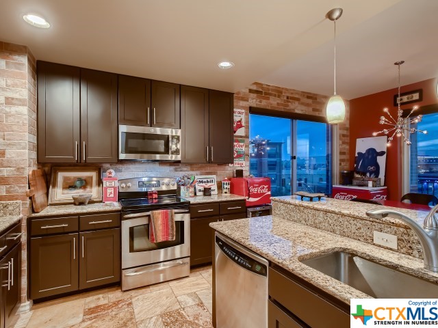 kitchen featuring stainless steel appliances, dark brown cabinetry, sink, light stone counters, and decorative light fixtures