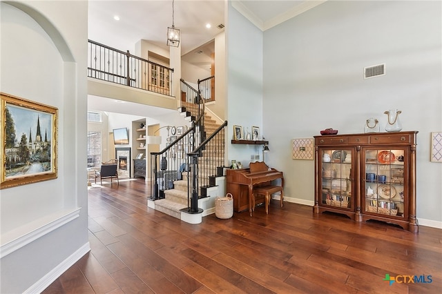 entryway featuring a high ceiling, wood finished floors, a warm lit fireplace, baseboards, and stairway