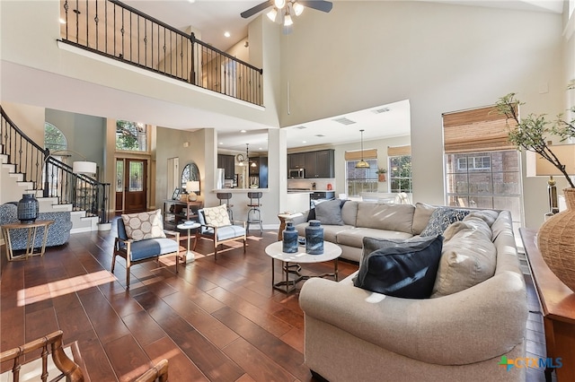 living room featuring ceiling fan, a high ceiling, stairway, and dark wood-style flooring