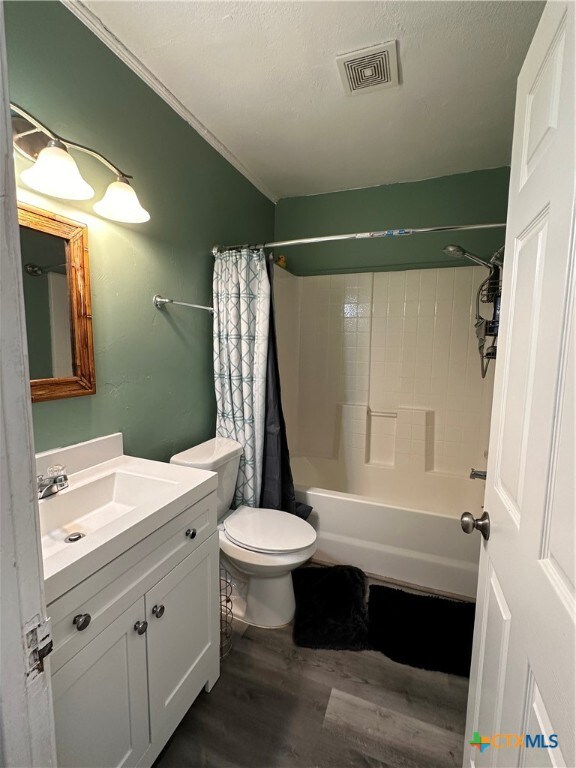 full bathroom featuring vanity, shower / tub combo, toilet, hardwood / wood-style flooring, and crown molding