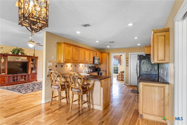 444 E Maxwell Ditch Rd, Port Lavaca, TX 77979 - kitchen with appliances with stainless steel finishes, dark countertops, light wood-style floors, backsplash, and a breakfast bar area