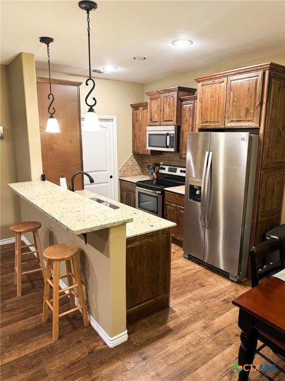 kitchen featuring sink, light stone counters, a kitchen breakfast bar, pendant lighting, and stainless steel appliances