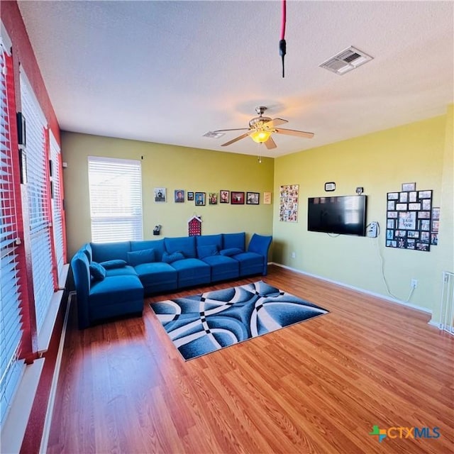 living room featuring baseboards, visible vents, a ceiling fan, wood finished floors, and a textured ceiling