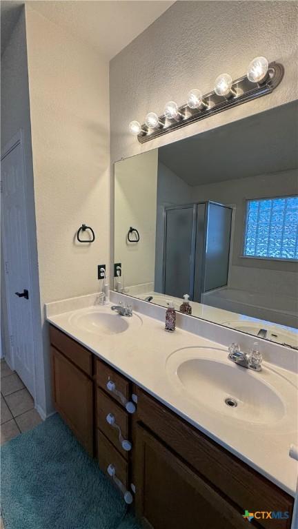 bathroom featuring double vanity, a stall shower, a sink, and tile patterned floors