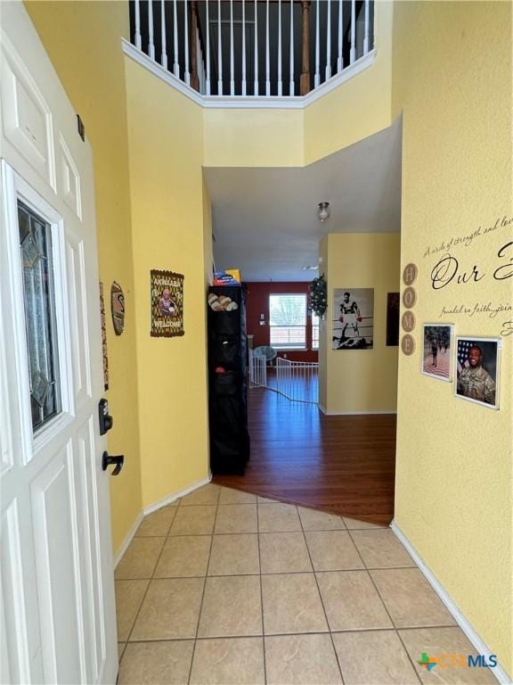 hallway featuring baseboards, a high ceiling, and light tile patterned floors