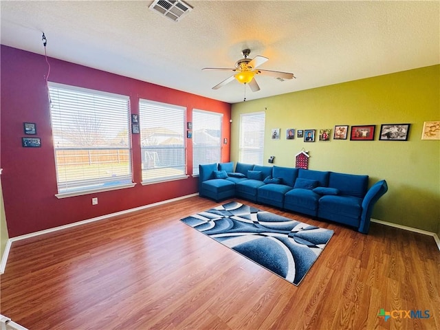 living room featuring a ceiling fan, visible vents, a textured ceiling, and wood finished floors