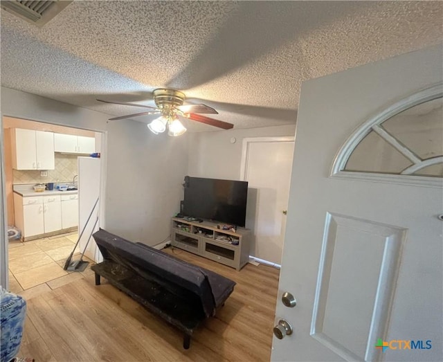 living room featuring a textured ceiling, light hardwood / wood-style floors, and ceiling fan