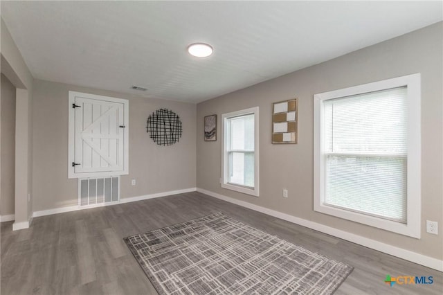 empty room with baseboards, visible vents, dark wood-style flooring, and a healthy amount of sunlight