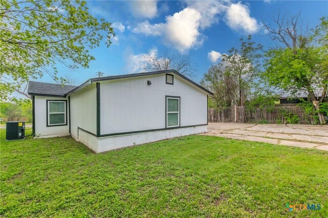 view of property exterior with central AC unit, fence, and a yard