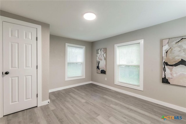 spare room featuring a wealth of natural light, light wood-type flooring, and baseboards