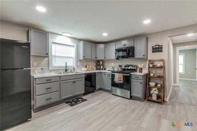 kitchen featuring light countertops, gray cabinets, a sink, light wood-style floors, and black appliances