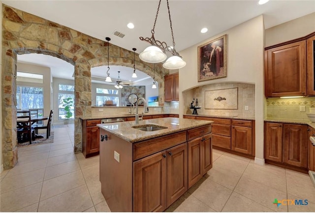 10510 Teich Loop, New Braunfels, TX 78132 - kitchen featuring light stone countertops, a sink, arched walkways, an island with sink, and backsplash