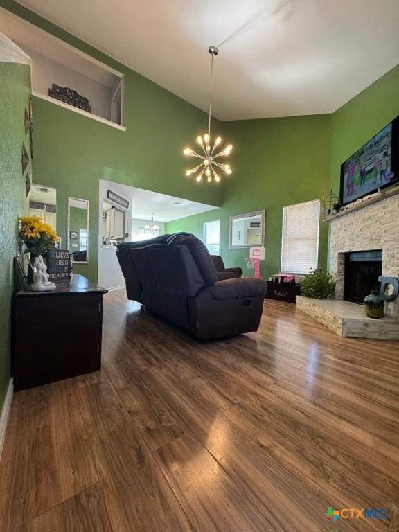 living room featuring an inviting chandelier, hardwood / wood-style flooring, a stone fireplace, and high vaulted ceiling