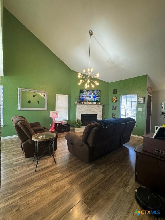 living room with an inviting chandelier, hardwood / wood-style flooring, a stone fireplace, and high vaulted ceiling