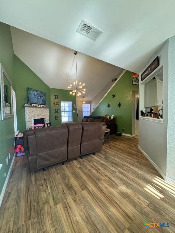 living room featuring vaulted ceiling, a stone fireplace, a chandelier, and hardwood / wood-style floors