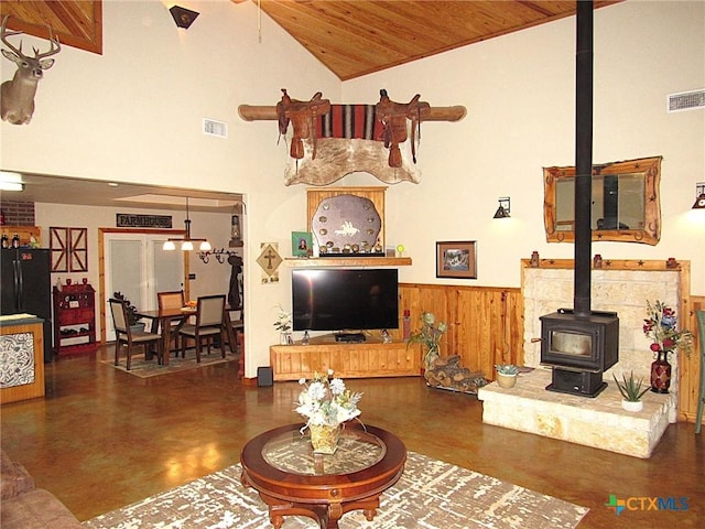 living room with high vaulted ceiling, a wood stove, wood ceiling, and wood walls