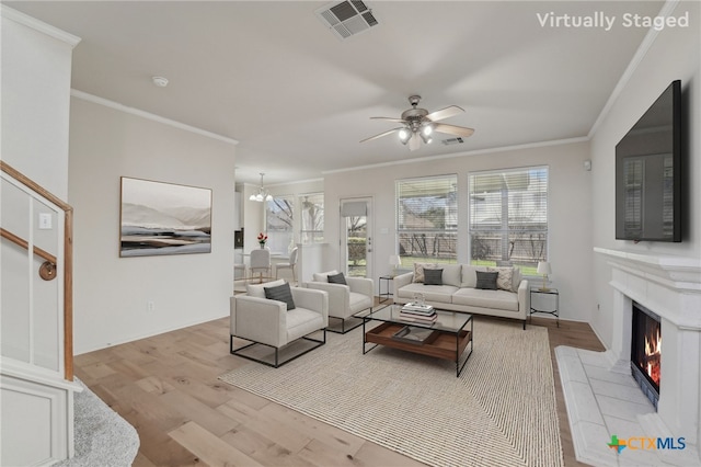 living room featuring a tiled fireplace, visible vents, crown molding, and wood finished floors