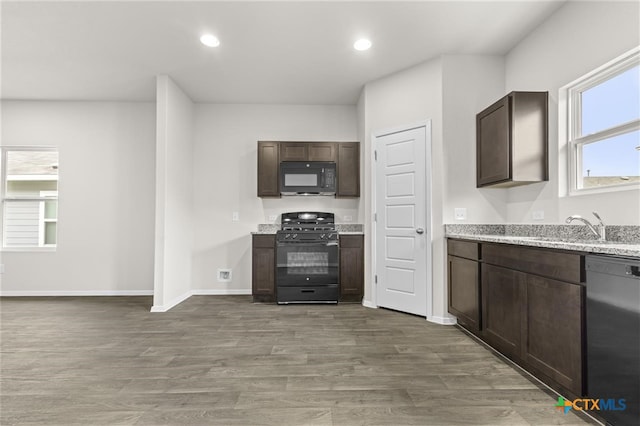 kitchen featuring sink, light stone counters, wood-type flooring, dark brown cabinets, and black appliances