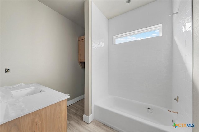 bathroom featuring baseboards, bathtub / shower combination, wood finished floors, and vanity