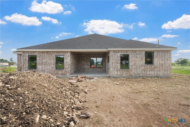 back of house featuring brick siding, roof with shingles, and a patio