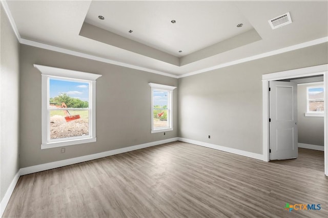 unfurnished room with visible vents, baseboards, wood finished floors, and a tray ceiling