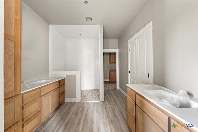 full bath with a shower, baseboards, wood finished floors, and two vanities