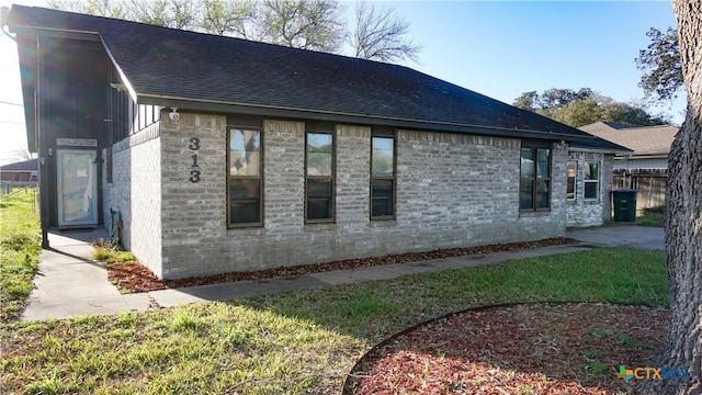 view of property exterior with a shingled roof, fence, and brick siding