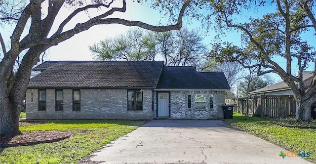 view of front of property featuring brick siding, concrete driveway, a front lawn, and fence