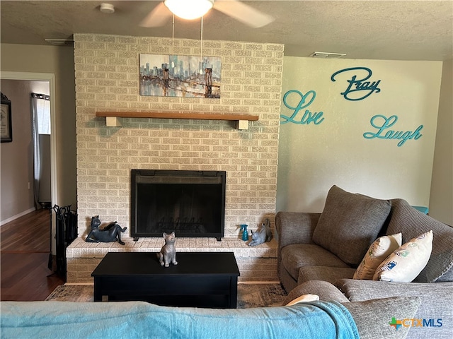 living room featuring a brick fireplace, a textured ceiling, wood-type flooring, and ceiling fan