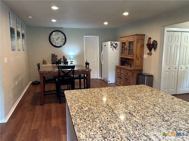 kitchen with dark hardwood / wood-style floors, light stone counters, and white fridge