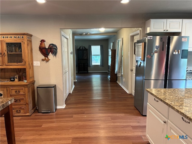 kitchen featuring stainless steel fridge, white cabinetry, light wood-type flooring, and light stone counters