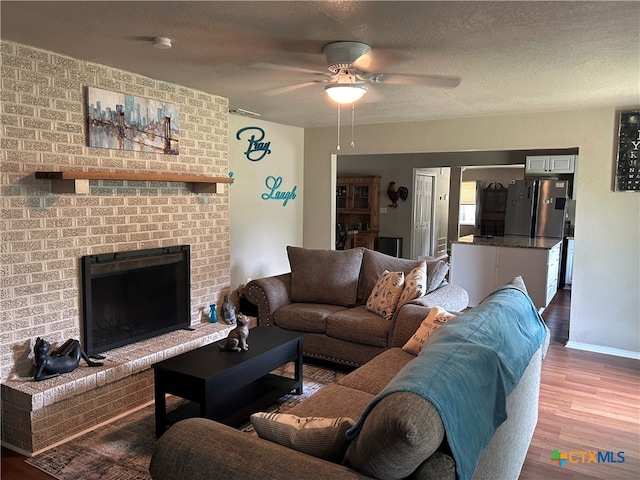 living room with a textured ceiling, hardwood / wood-style flooring, ceiling fan, and a brick fireplace