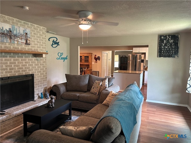 living room with a textured ceiling, hardwood / wood-style floors, a brick fireplace, and ceiling fan