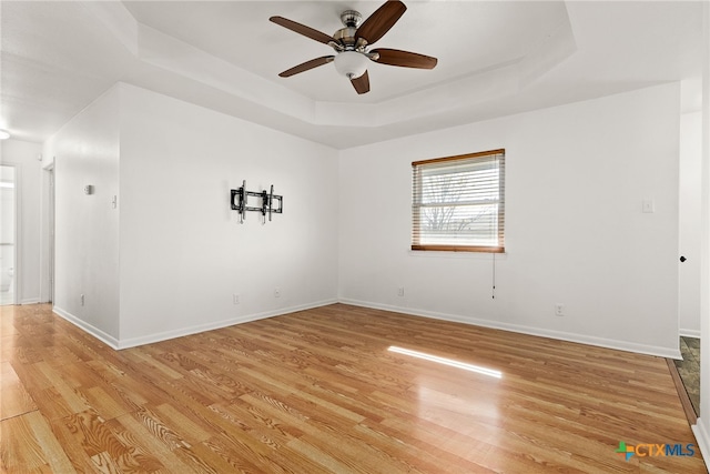 spare room with a raised ceiling, ceiling fan, and light wood-type flooring