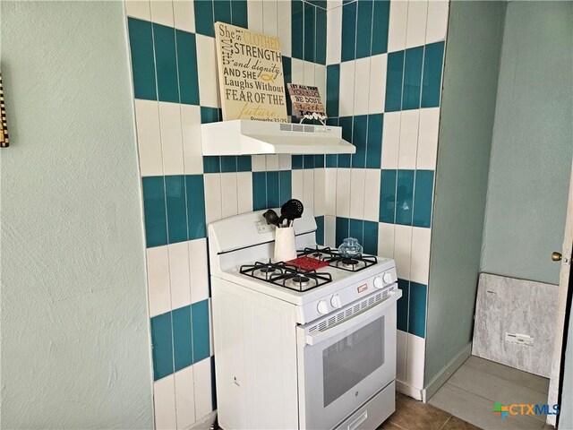 703 Atkinson Ave, Killeen, TX 76541 - kitchen with white gas range oven, under cabinet range hood, a textured wall, tile walls, and tile patterned floors