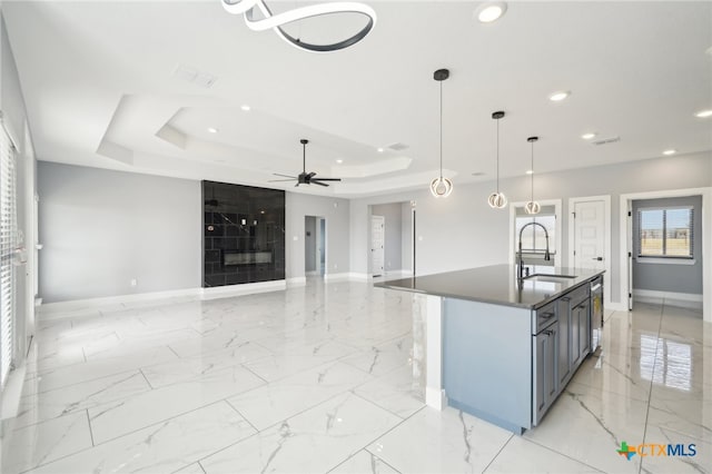 kitchen featuring a kitchen island with sink, a raised ceiling, sink, hanging light fixtures, and ceiling fan