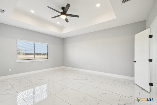 empty room with ceiling fan and a tray ceiling