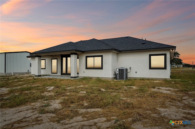 back house at dusk featuring a lawn and cooling unit