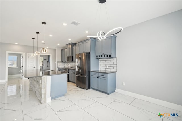 kitchen with sink, stainless steel appliances, backsplash, decorative light fixtures, and a center island with sink