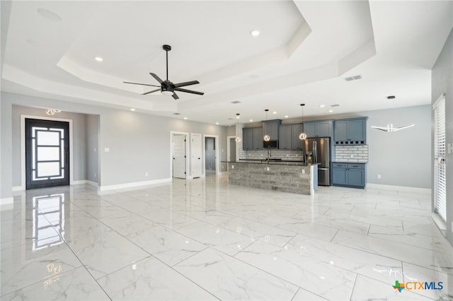 unfurnished living room with a raised ceiling, ceiling fan, and sink