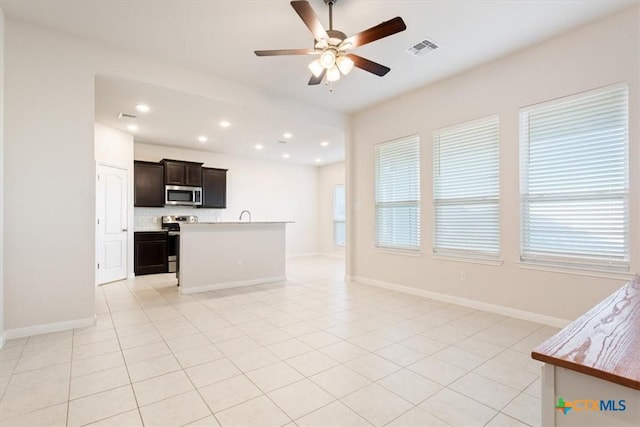 kitchen featuring ceiling fan, tasteful backsplash, a center island with sink, light tile patterned flooring, and stainless steel appliances