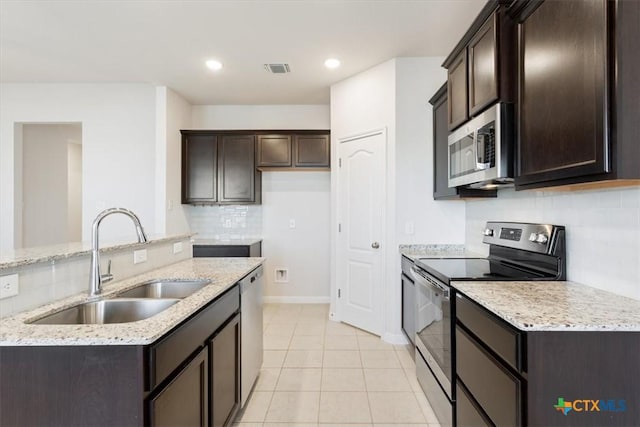 kitchen with light tile patterned floors, stainless steel appliances, light stone countertops, dark brown cabinetry, and sink