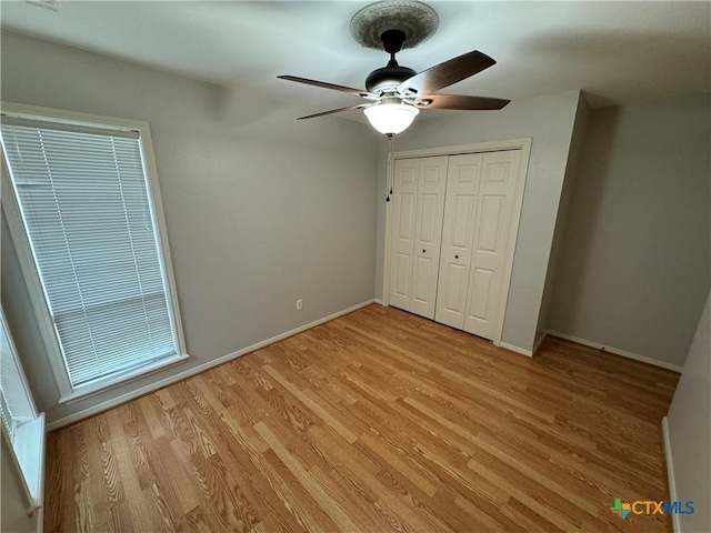 unfurnished bedroom with light wood-style floors, a closet, baseboards, and a ceiling fan