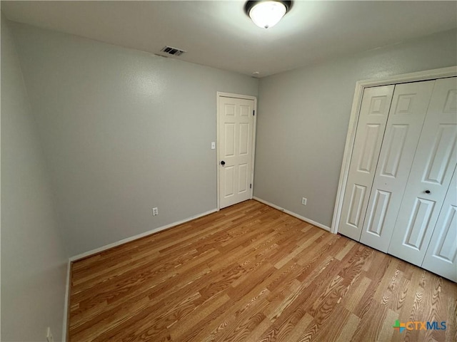 unfurnished bedroom featuring light wood-style flooring, a closet, visible vents, and baseboards