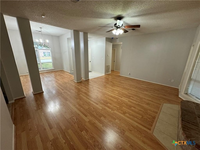 unfurnished living room featuring a textured ceiling, visible vents, wood finished floors, and ceiling fan with notable chandelier