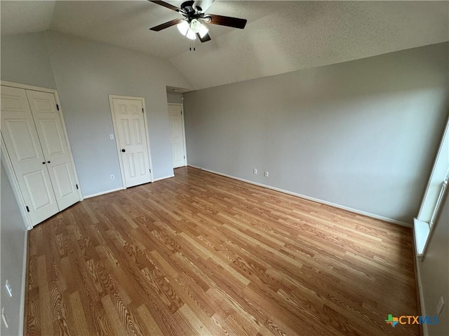 unfurnished bedroom featuring lofted ceiling, light wood-type flooring, two closets, and a ceiling fan