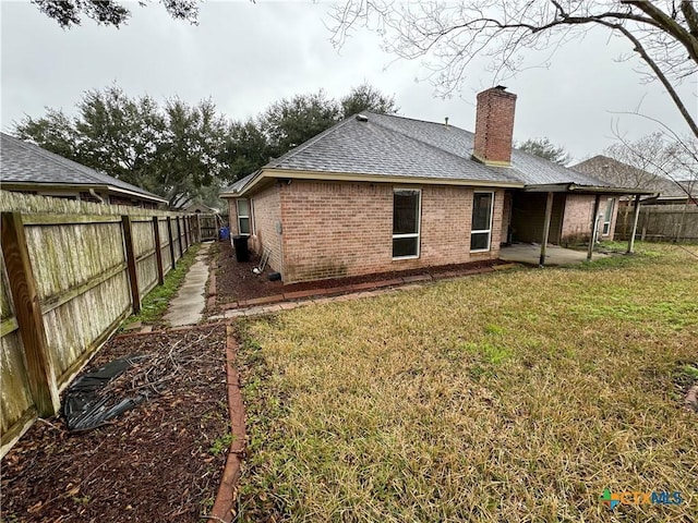 back of property featuring a yard, a fenced backyard, roof with shingles, and brick siding